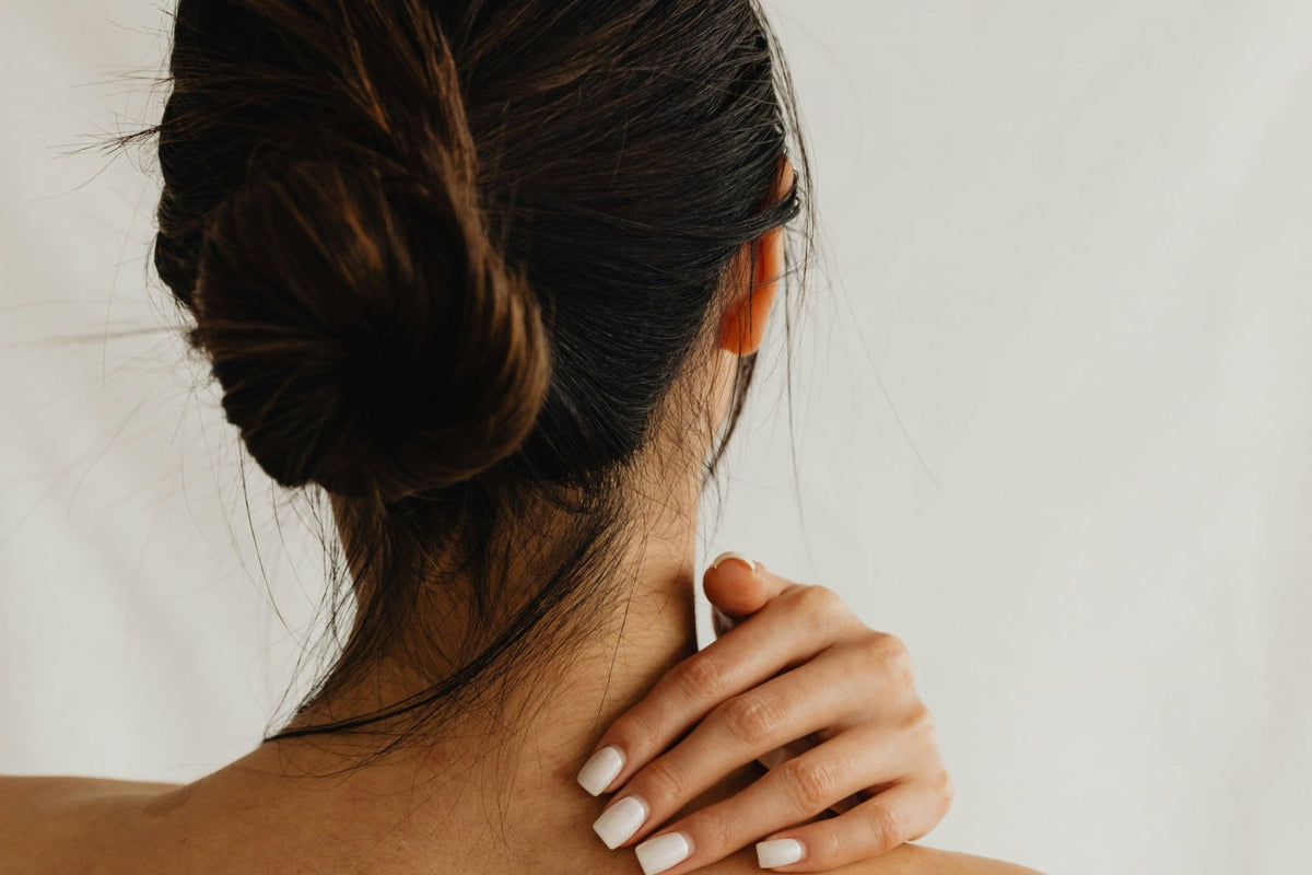 Frau von hinten mit Hand im Nacken vor hellem Hintergrund