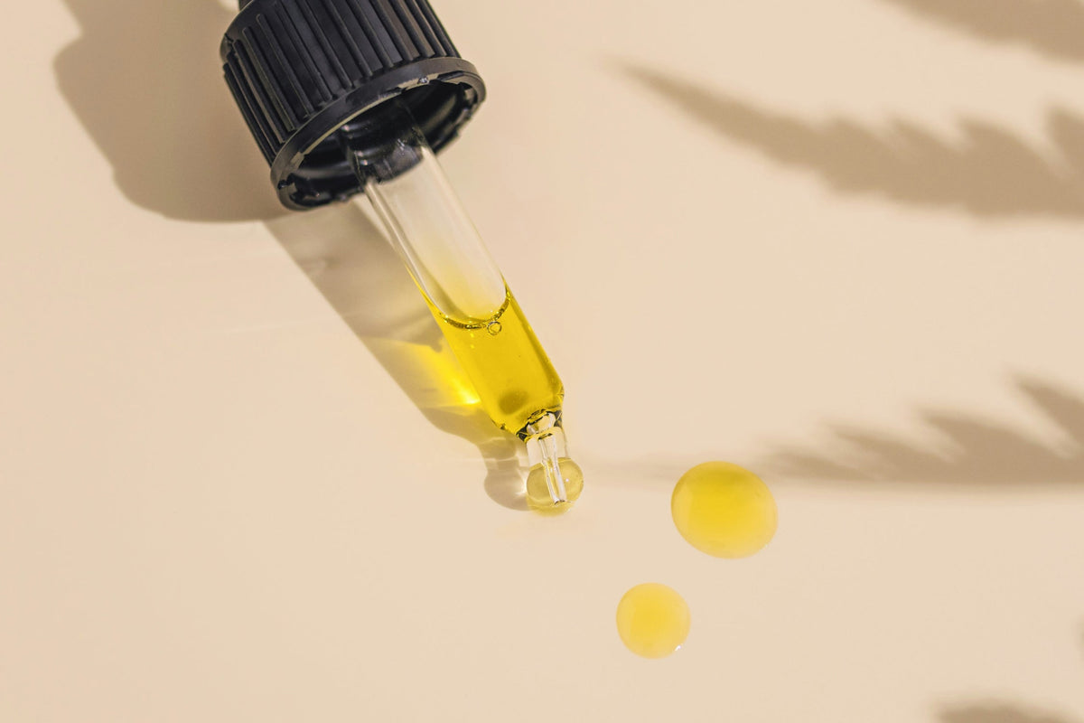 Pipette mit goldgelbem Pflanzenöl und zwei Öltropfen auf hellem Hintergrund