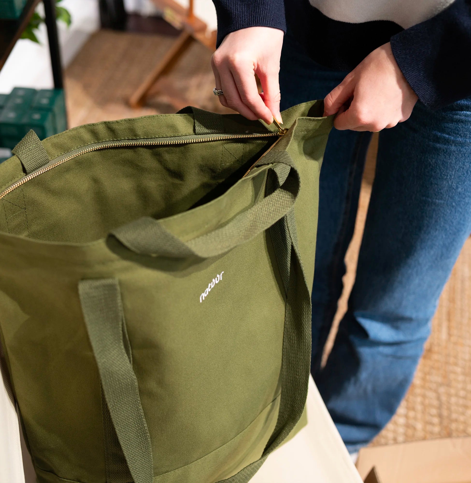 Person öffnet den Reißverschluss einer grünen Natuur-Tragetasche, die aus nachhaltigem Material besteht, geeignet für umweltbewusste Einkäufe und Alltag.