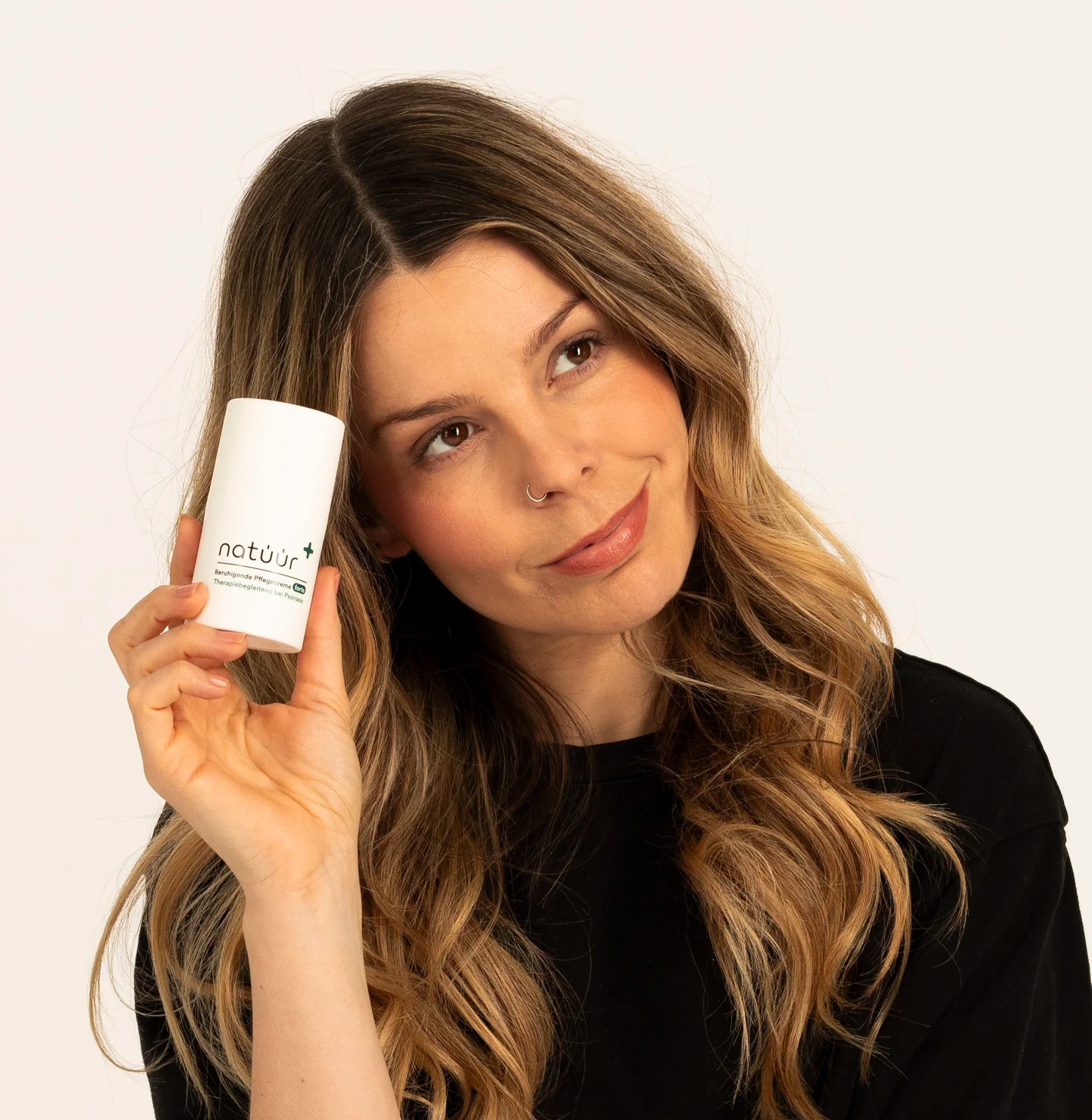 Man sieht eine Frau. It schwarzen T-Shirt und langen braunen Haaren. Sie hat ihren Kopf leicht gebeugt und hält in ihrer Hand die natüür Cream forte.
