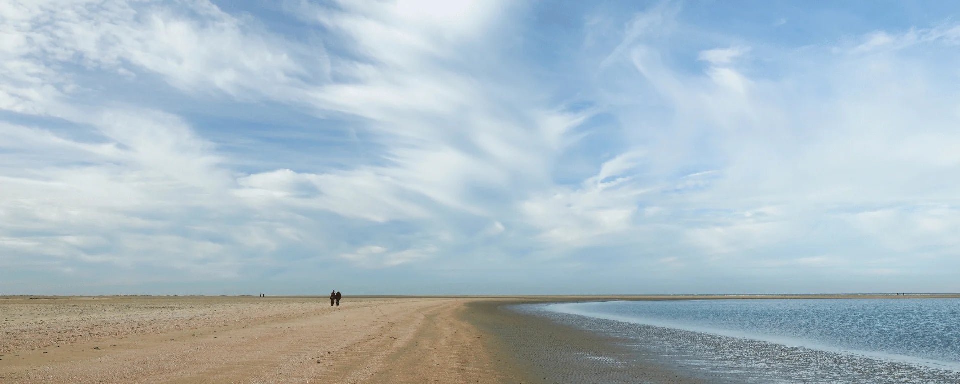 Man sieht den braunen Sandstrand, sowie das blaue Wasser der Nordee. Der Himmel ist hellblau und mit ein paar seichten, weißen Wolken bedeckt. 