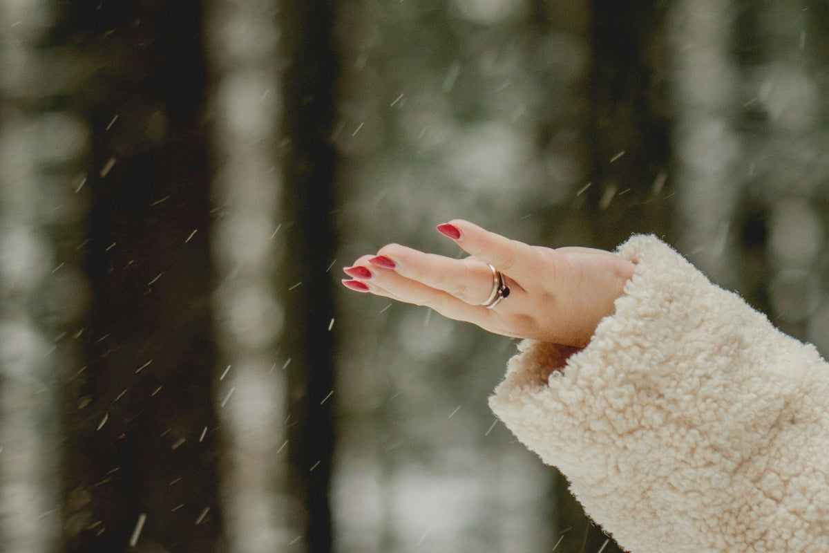 Hand im Schneefall vor verschneitem Wald