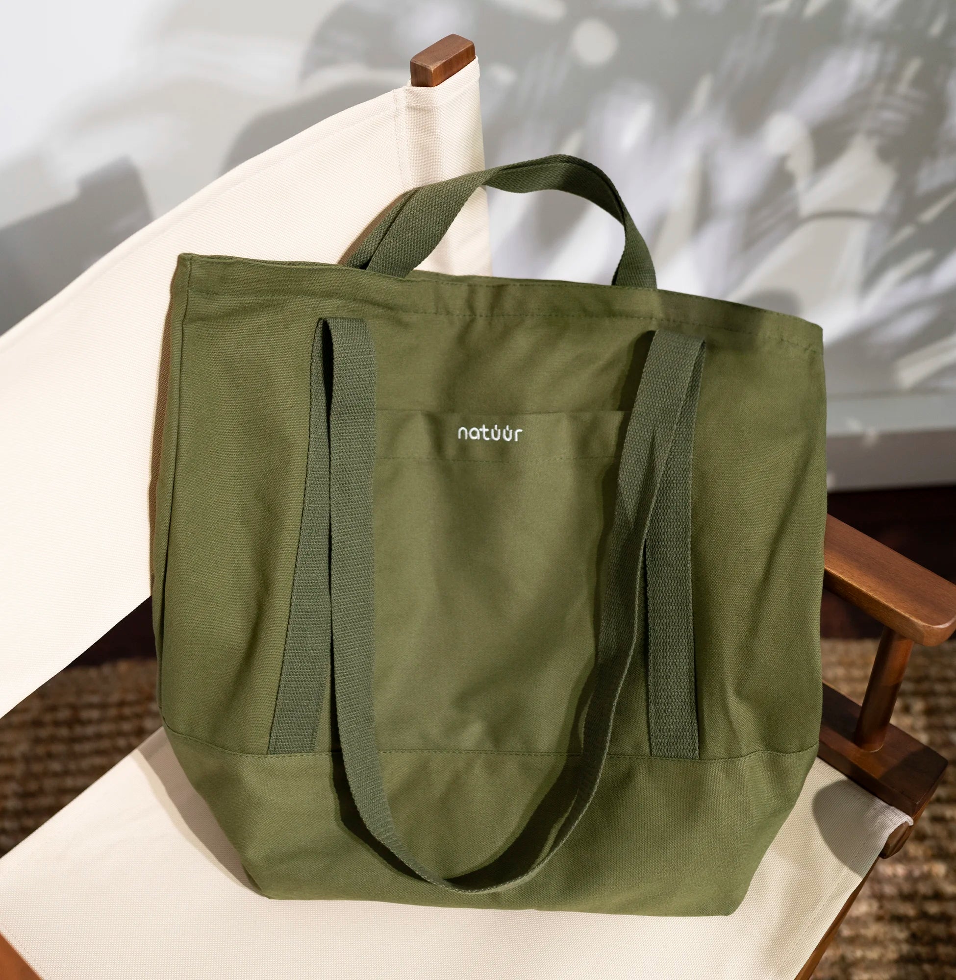 Grüne Natuur-Tragetasche aus nachhaltigem Material, stilvoll auf einem cremefarbenen Stuhl platziert, ideal für umweltbewusste Mode und Einkauf.